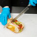 A person wearing blue gloves cutting a sandwich with a Dexter-Russell V-Lo scalloped bread and sandwich knife.