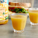 Two glasses of pineapple juice next to a sandwich on a table.
