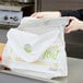 A woman in a kitchen putting a foil pan into a plastic LK Packaging take out bag.