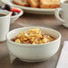 An Acopa ivory stoneware bowl filled with oatmeal and fruit on a table with a cup of coffee.