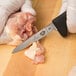 A person in gloves using a Victorinox poultry boning knife to cut chicken on a cutting board.