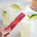 A hand holding a red 1-part "Liquor" raffle ticket next to a glass of red liquid with a lime wedge.