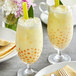 Two glasses of yellow Fanale pineapple milk tea with green straws and leaves.