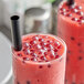 A glass of red liquid with Fanale Raspberry Popping Boba and a black straw on a white surface.