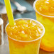 A couple of plastic cups of orange mango drinks with straws.