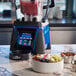 A Waring commercial blender on a counter next to a bowl of fruit and nuts.