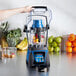 A Waring commercial blender with a blue lid and container on a table full of fruit.