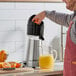 A man using the Avamix stainless steel citrus bar juicer to make orange juice on a counter.