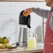 A man using an AvaMix citrus juicer to pour lemon juice into a pitcher.