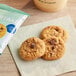 A package of Partake Gluten-Free Soft Baked Chocolate Chip Cookies on a table with a napkin of cookies and a cup of coffee.