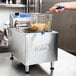 A hand using a basket to fry food in a Globe electric countertop fryer.