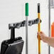 A white wall with a Lavex wall-mount tool holder holding broom and cleaning tools.