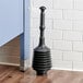 A black Lavex toilet plunger on a wood floor.