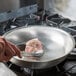 A person using tongs to cook a steak in a Vollrath aluminum fry pan.