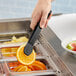 A hand using Cambro black plastic tongs to pick up a slice of watermelon.