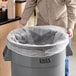 A man holding a Lavex high density garbage bag over a large garbage can.