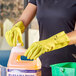 A person wearing Lavex yellow rubber gloves holding a jug of cleaning liquid.