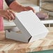 A person opening a white corrugated bakery box with a lid