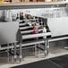 A Regency stainless steel five-tiered liquor display rack on a bar counter filled with bottles and glasses.