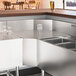 A stainless steel counter with a Regency Spec Line 90-degree angle inside corner underbar filler.