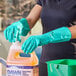 A person wearing Lavex green dishwashing gloves putting cleaning liquid in a plastic jug.