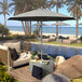 A patio area with a pool, chairs, and a table with a California Umbrella granite umbrella above the table.