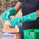 A person wearing Lavex green unlined nitrile gloves putting cleaning liquid in a plastic jug.
