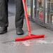 A person using a Vikan red single blade rubber floor squeegee to clean the floor.
