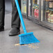 A person using a Vikan blue broom to sweep up food on the floor.