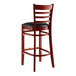 A Lancaster Table & Seating mahogany wood bar stool with black vinyl seat.