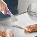 A gloved hand uses a Choice spatula with a purple handle to cut meat on a white surface.