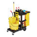 A janitor cart with shelves, a yellow vinyl zippered bag, and cleaning supplies including a mop bucket and caution sign.