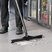 A person cleaning a floor with a Vikan black single blade rubber floor squeegee.