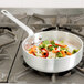 A Vollrath Wear-Ever saute pan full of vegetables cooking on a stove.