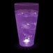 A 20 oz. plastic cup with a purple LED light filled with purple liquid on a bar counter.