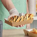 A person holding a tray of waffles in Carnival King medium foiled paper food trays.