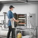 A person wearing an apron putting food into a Cooking Performance Group electric combi oven.