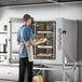 A man in an apron holding trays of food in a Cooking Performance Group electric combi oven.