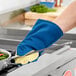 A person using a Tucker Safety oven mitt to hold a pan over a stove.