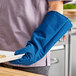 A person wearing a blue Tucker Safety Products oven mitt holding a tray of food.