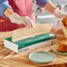 A person wearing gloves using EcoChoice natural kraft wax paper to wrap food on a plate.