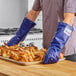 A person wearing Tucker Safety blue and yellow gloves holding a tray of chicken.