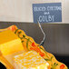 A American Metalcraft double-sided sign clip holding a sign that says "cheese" on a plate of yellow and white cheese.