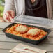 A woman holding a Choice rectangular black plastic microwavable container filled with spaghetti and meatballs.