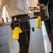 A black Ergodyne Arsenal server apron pouch with multiple pockets and a yellow cloth attached.