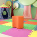 An orange Flash Furniture Nicholas moon-shaped ottoman in a colorful playroom with a toy tent.