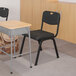 A black Flash Furniture Hercules plastic chair next to a school desk.