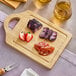 A Franmara rubberwood cutting board with cheese and fruit on it.