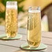 Two Franmara Tritan plastic stemless champagne flutes filled with champagne on a table with coasters.