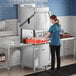A woman in a blue uniform operating a Noble Warewashing high temperature door type dishwasher.